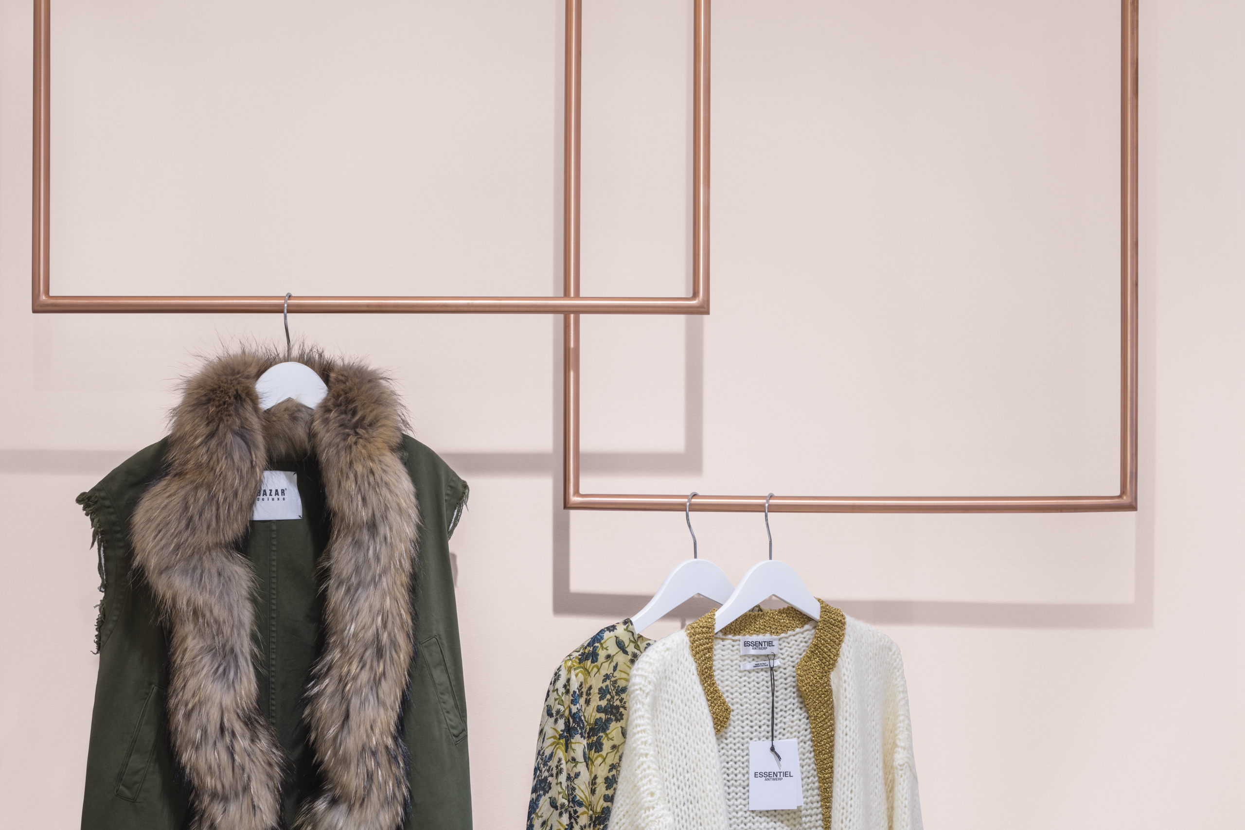 Clothing display at Spazio Boutique with copper-toned frames against a soft pink wall